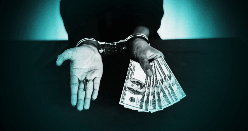 hands with handcuffs on holding key in one hand and money in other