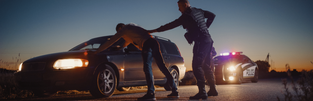 police officer arresting man with hands on car