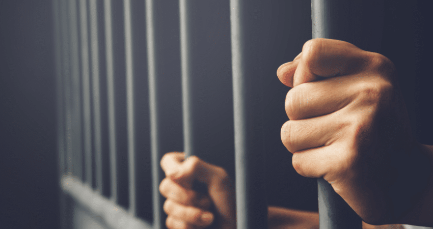 man in jail holding cell bars