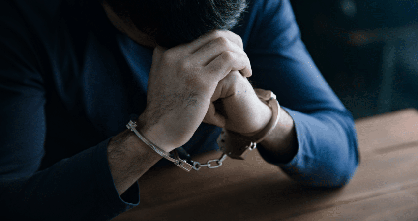 man in handcuffs resting head on hands stressed
